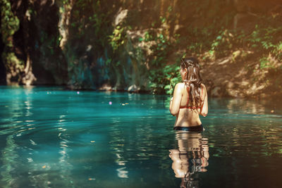 Rear view of young latina woman standing in blue green waters of rio blanco in costa rica