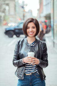 Portrait of smiling young woman holding disposable cup in city