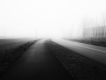 Road amidst bare trees in foggy weather