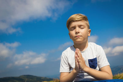 Small boy in namaste pose meditating with eyes closed in nature against the sky. copy space.