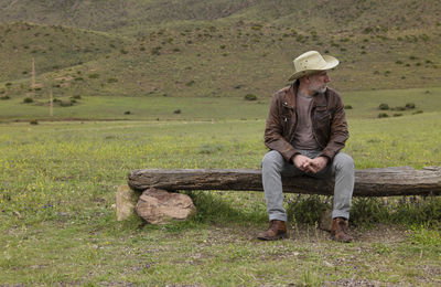Adult man in cowboy hat sitting on wooden bench in field