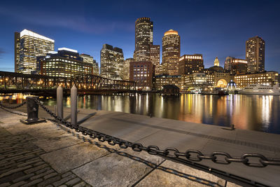 Illuminated buildings by river against sky in city at night