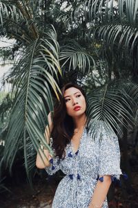 Thoughtful young woman standing against plants in park