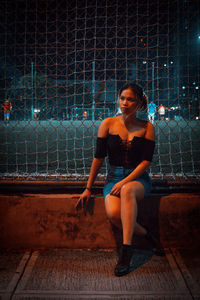 Portrait of a young woman sitting on chainlink fence