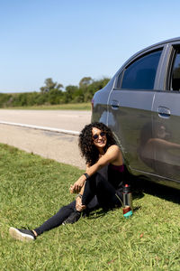 Woman sitting next to her car while relaxing during a road trip.