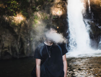 Full length of man standing in water and smoke vape 