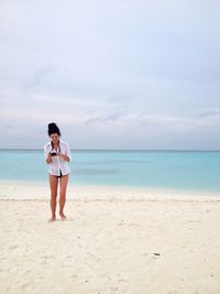 Full length of sensuous woman standing at beach against sky