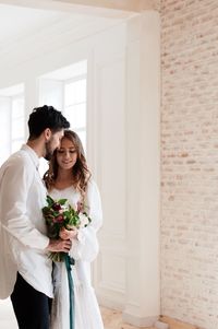 Couple holding bouquet while standing in room during wedding ceremony