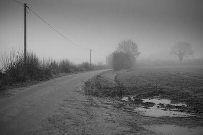 Road amidst field against clear sky during winter