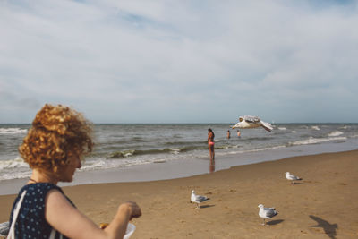 Woman feeding seagulls at beach against sky
