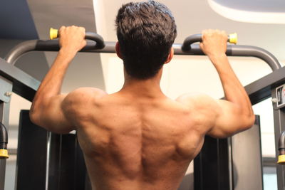 Rear view of shirtless young man exercising in gym