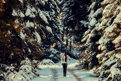 Woman standing on snow covered road amidst trees