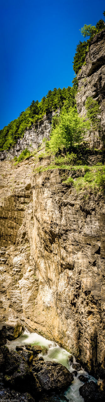 rock - object, nature, rock formation, beauty in nature, no people, tranquil scene, scenics, waterfall, blue, geology, tranquility, mountain, clear sky, day, outdoors, sunlight, sky, water, low angle view, physical geography, tree, landscape, motion, holiday