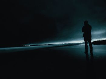 Silhouette man standing on beach against sky at night