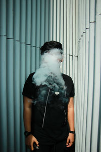 Young man smoking against wall