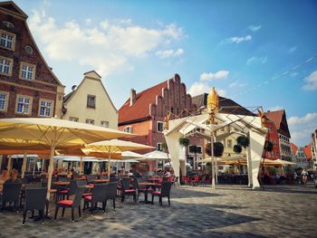 Chairs and tables in cafe by buildings in city against sky