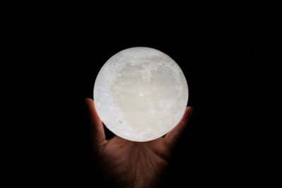 Close-up of hand holding crystal ball against black background