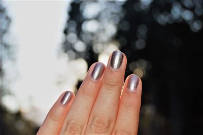 Cropped hand of woman with painted nails against tree