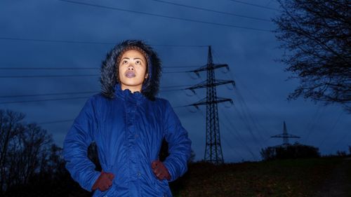 Woman looking up against electricity pylon at night