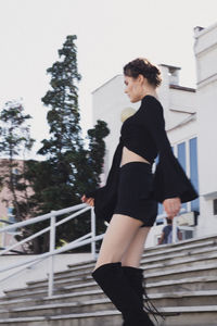 Side view of young woman standing against railing