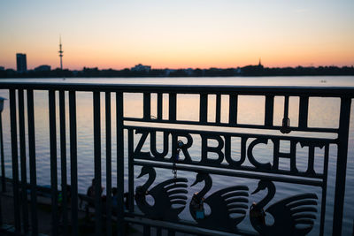 Silhouette railing by river against clear sky during sunset