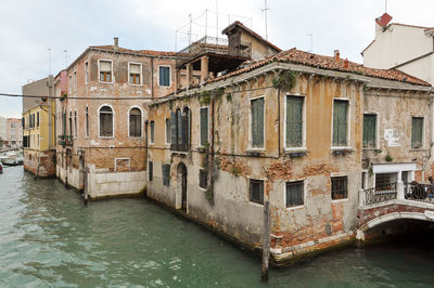 Canal by old building against sky