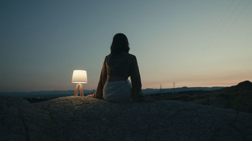 Rear view of woman standing against sky during sunset