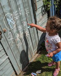 Toddler playing with chalk on fence. 