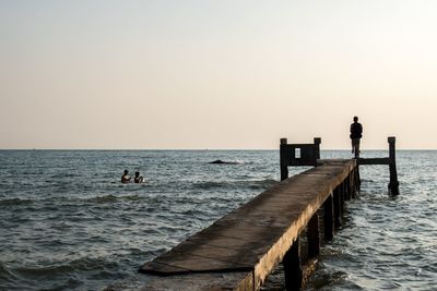 Silhouette men fishing in sea against clear sky