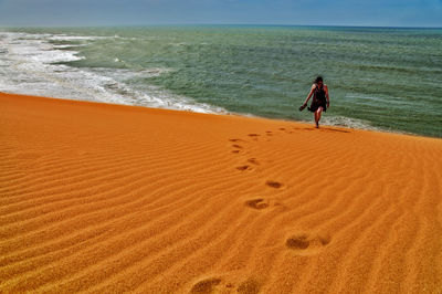 Woman walking on sand dune against sea