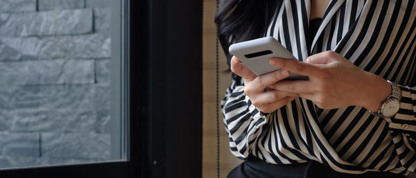 Midsection of man using mobile phone while standing on window