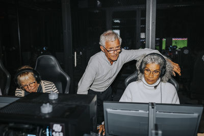 Elderly woman playing video game on computer by male and female friends at gaming lounge