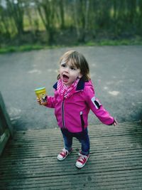 Cute girl holding drink while standing on footpath