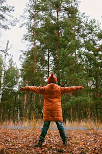 Girl in orange coat with outstretched arms enjoys fresh air in fall forest. mental health, autumn