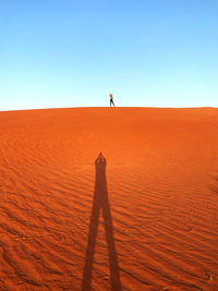 Rear view of man walking on beach against clear sky during sunset