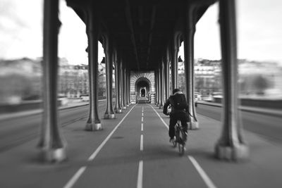 Rear view of man cycling below bridge