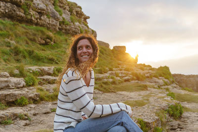 Portrait of smiling man sitting on rock against sky