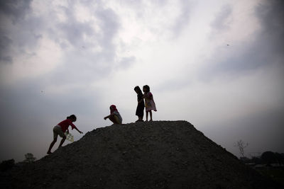 Low angle view of friends on cliff against cloudy sky