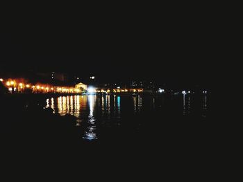 Illuminated buildings by river against sky at night