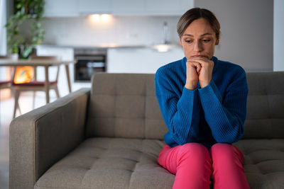 Young woman sits on sofa with depressed and tired expression after breaking up with boyfriend