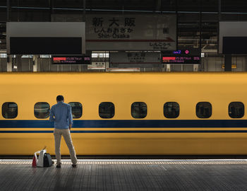 Rear view of man standing on illuminated railroad station platform