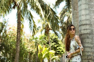 Portrait of young woman standing against palm trees