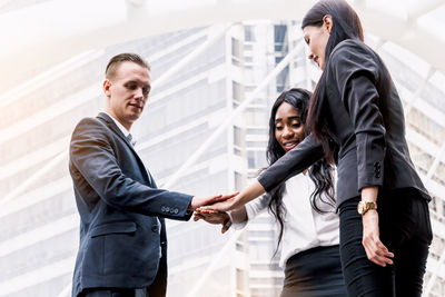 Business people stacking hands while standing against building