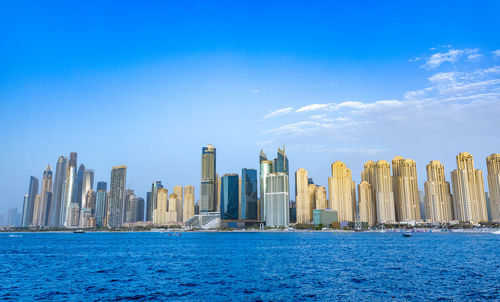 Buildings by river against blue sky