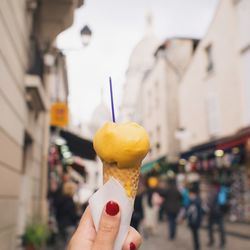 Cropped image of woman hand holding ice cream cone on street in city