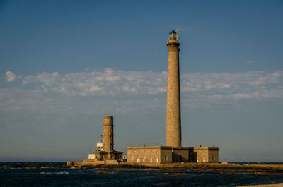 Lighthouse by building against sky