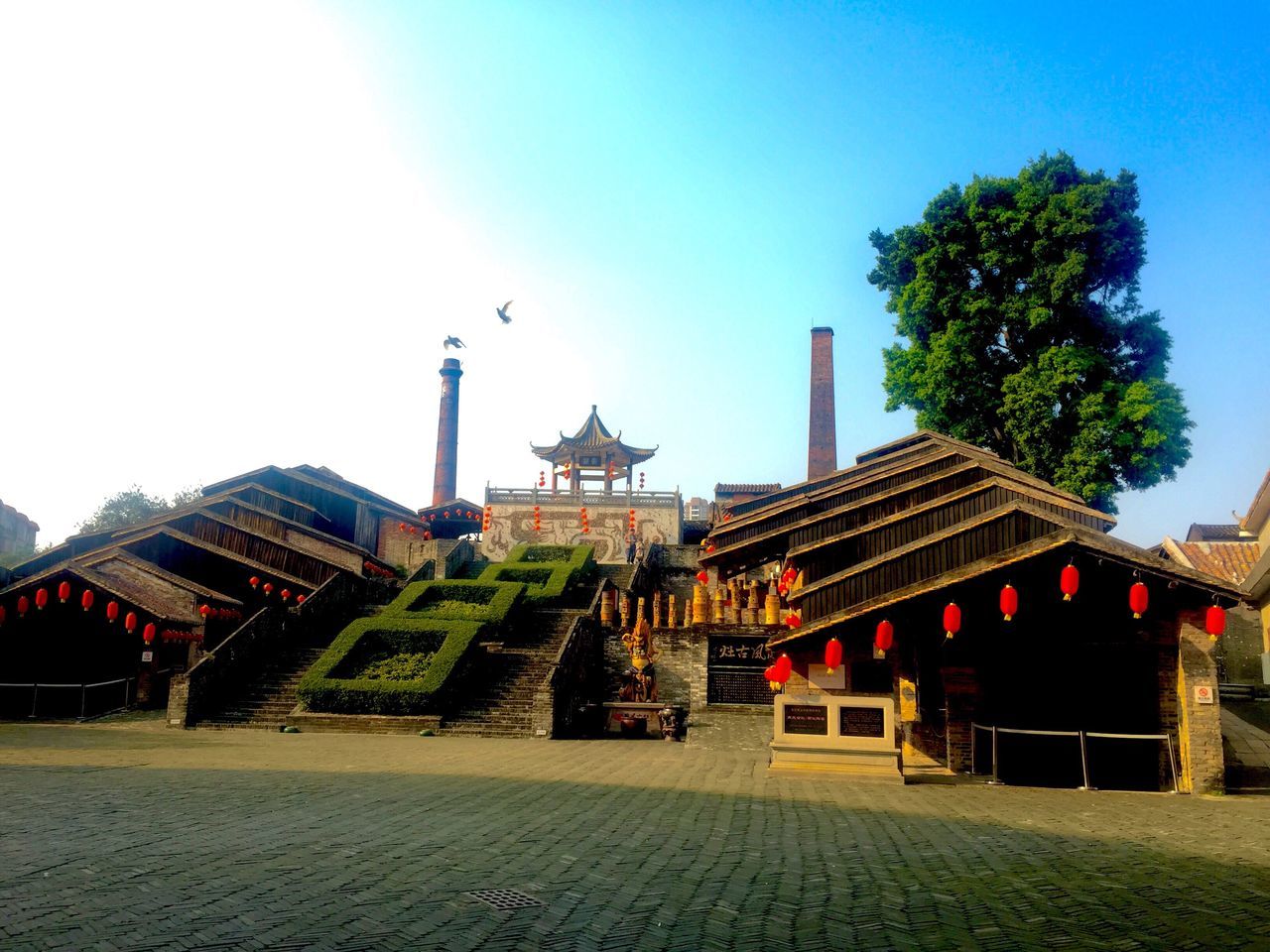 building exterior, architecture, built structure, clear sky, tree, sky, copy space, blue, incidental people, religion, place of worship, sunlight, flag, day, house, outdoors, roof, road, street