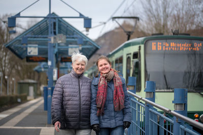 Portrait of smiling grandmother and granddaughter standing at railroad station platform