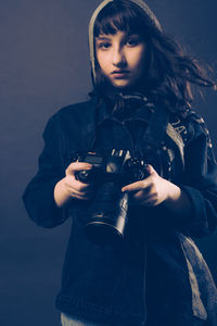 Portrait of young woman standing against black background