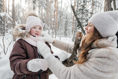 Mother helps her daughter on a walk in the snowy forest